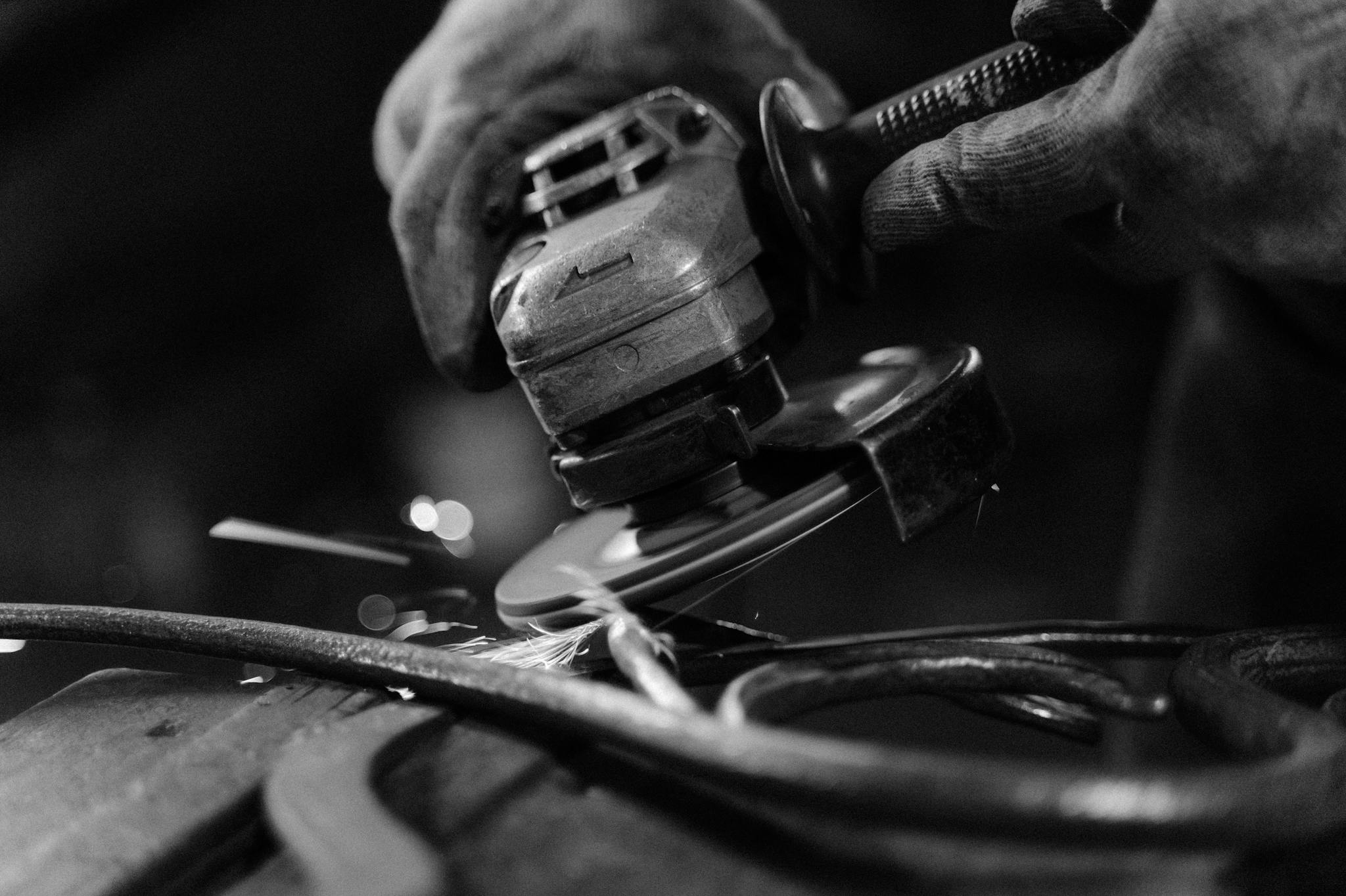 Black and white close-up of an angle grinder creating sparks on metal, showcasing craftsmanship.