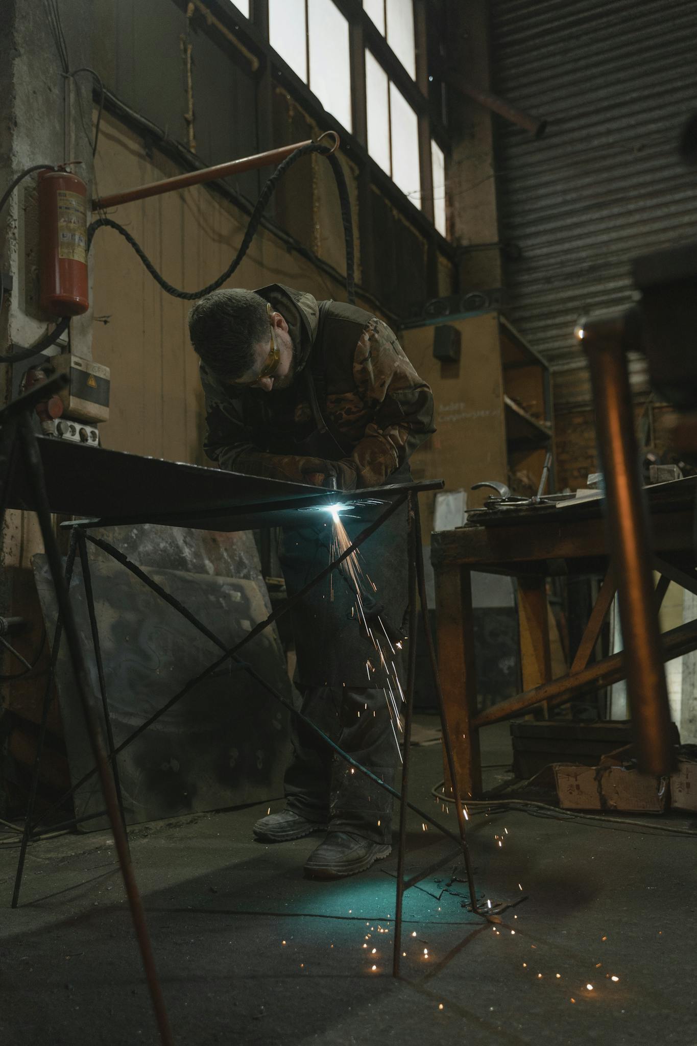 Close-up of a welder working on metal inside a factory with sparks flying.