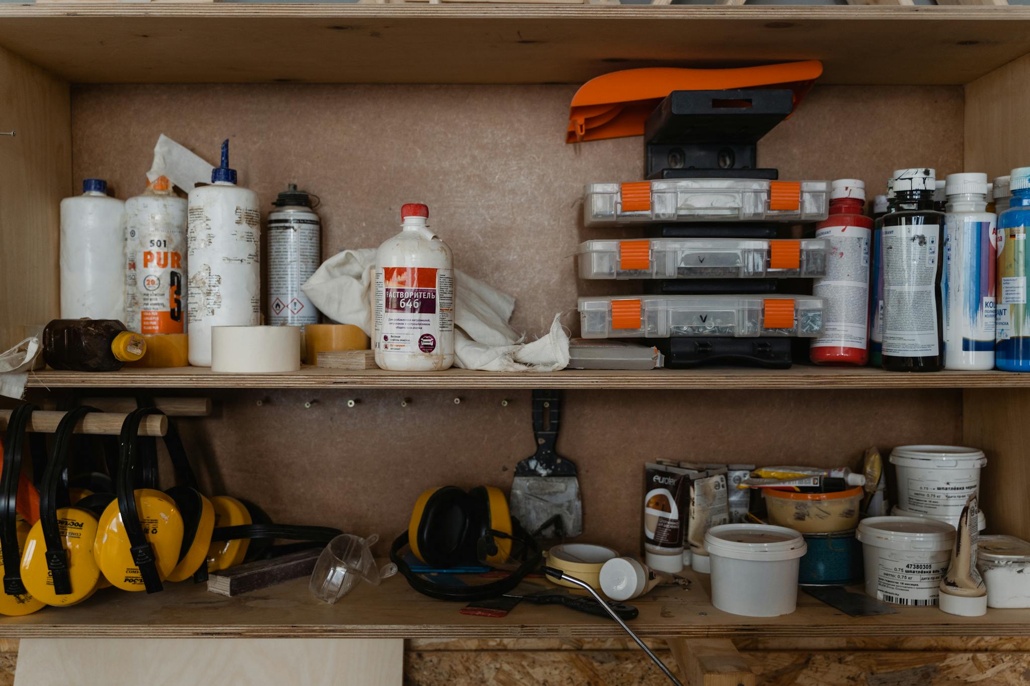 Wooden shelf with various tools, paint supplies, and safety gear in a workshop setting.